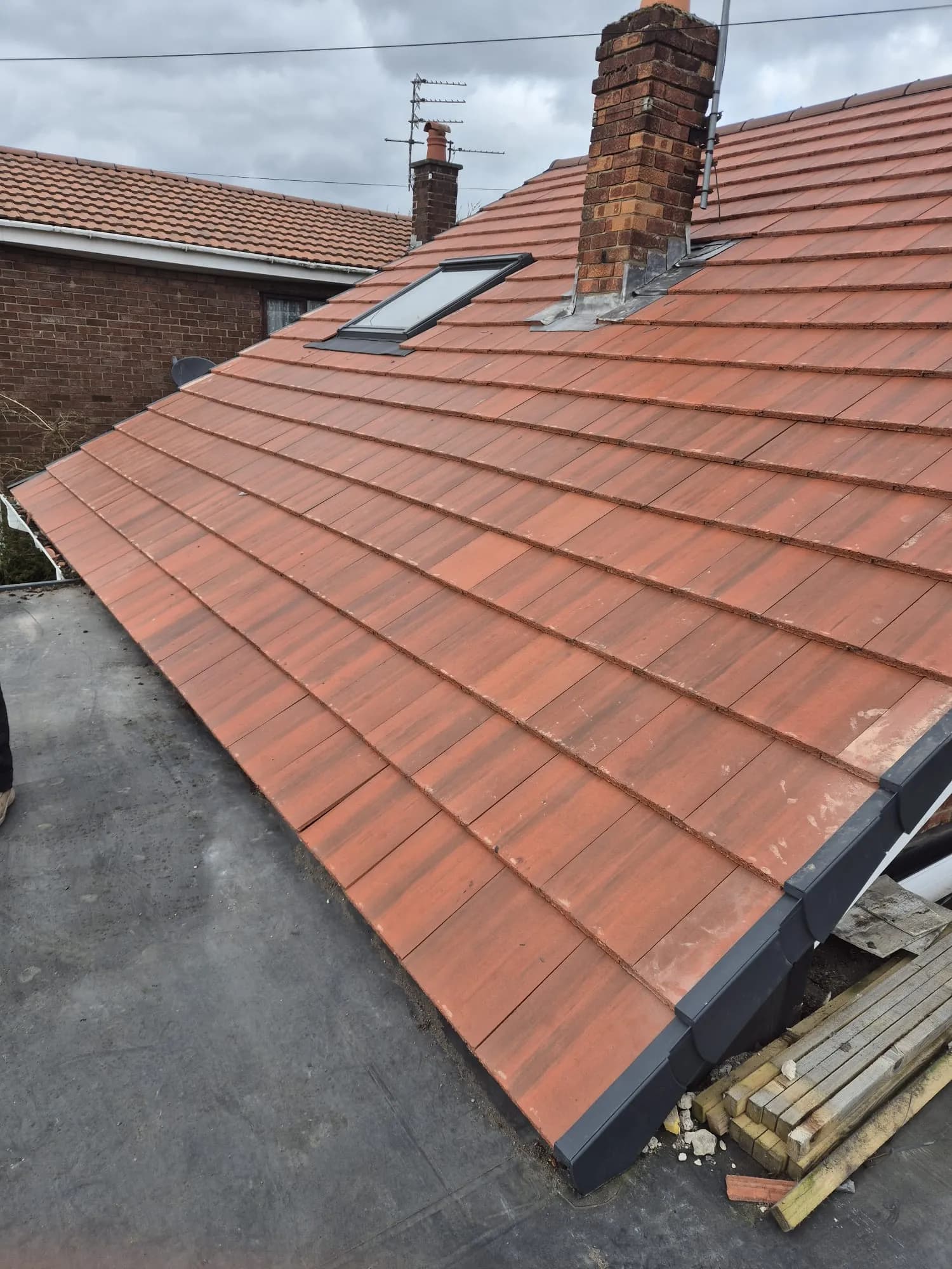 New red tiles on a lean-to roof beside a brick chimney and a roof light