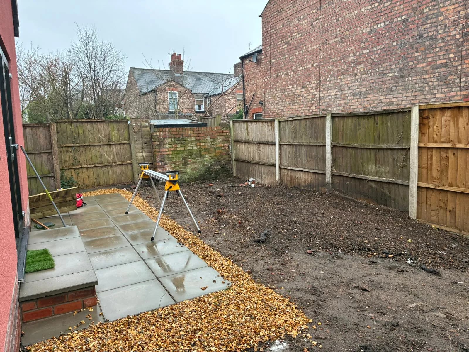 New grey slab paving laid beside the old fence, with a saw set up on its stand